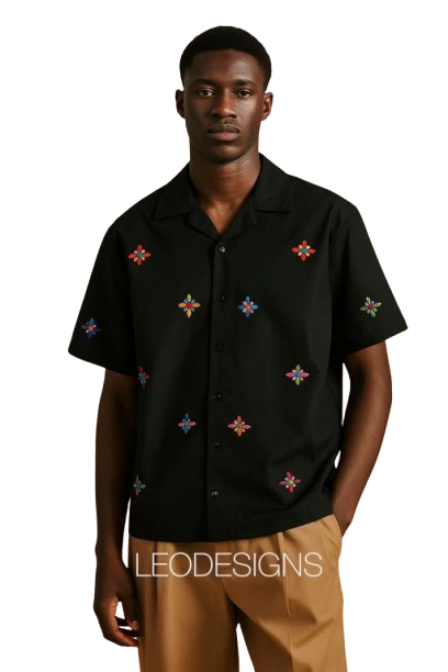  Man wearing black short-sleeve shirt with colorful floral embroidery and tan pants.